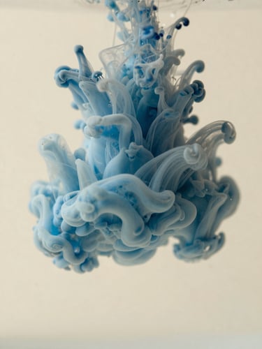 Macro photograph of soft blue ink swirling in warm cream water, diffused daylight, shallow depth of field, minimalist abstract style.