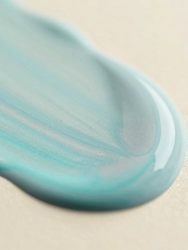 Macro close-up of soft cyan and mist gray fluid acrylic paint blending smoothly on a warm cream canvas, soft diffused daylight, shallow depth of field