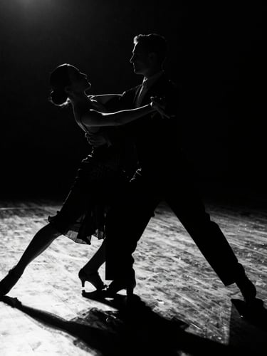 Dramatic high-contrast black and white shot of a ballroom dance couple in mid-motion, sharp silhouettes, polished dark wood floor reflecting light, 35mm
