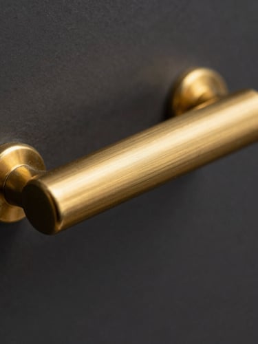 Macro close-up shot of a heavy-gauge solid brass cabinet handle, showing the exquisite brushed gold texture, sharp metallic highlights, and fine knurled details, shallow depth of field.