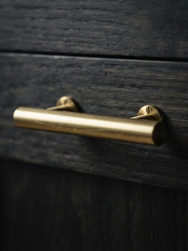 Macro shot of a brushed gold cabinet handle on dark oak wood, dramatic side lighting, sharp metallic highlights