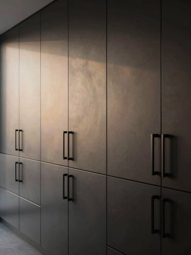Wide-angle architectural shot of a modern minimalist luxury kitchen, soft window light illuminating dark charcoal cabinets fitted with sleek matte black ELLIST handles.