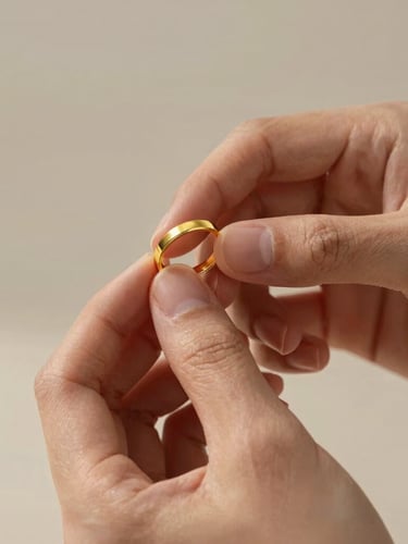 Close-up of elegant hands gently holding a gold ring under soft directional light, highlighting the metallic reflections and fine texture, minimalist background