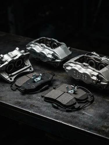 Pristine genuine Range Rover OEM brake pads and metallic calipers neatly arranged on a clean dark surface, low-key dramatic studio lighting with sharp metallic highlights, dark moody automotive photography style.
