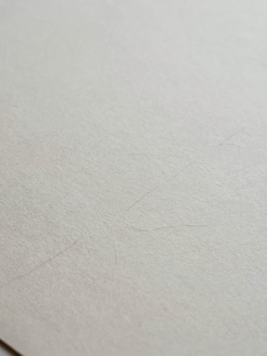 Extreme close-up of textured heavy handmade paper with faint fountain pen ink strokes, soft overcast natural light, desaturated slate tones, 35mm film grain