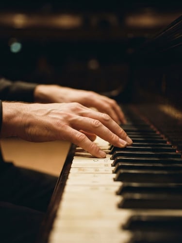 Close-up of a pianist's hands on physical piano keys, dramatic side-lighting, deep charcoal and warm amber tones, shallow depth of field.