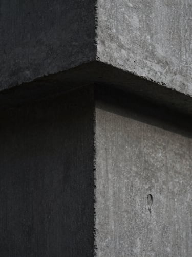 Extreme close-up of smooth, architectural raw concrete with subtle formwork lines, dramatic side-lighting casting deep shadows, highlighting the fine grain and monolithic texture, 35mm lens.