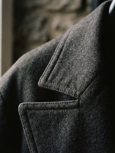 Extreme close-up of a 1990s Japanese designer wool gabardine coat collar, showing precise structural stitching, soft directional natural light, desaturated muted tones, sharp focus, 35mm film.