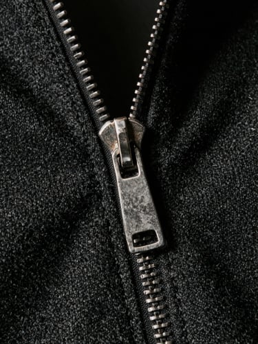 Extreme close-up of a vintage metal zipper and pristine double-stitching on heavy black wool gabardine, soft directional natural light, desaturated muted tones, sharp focus, 35mm film.