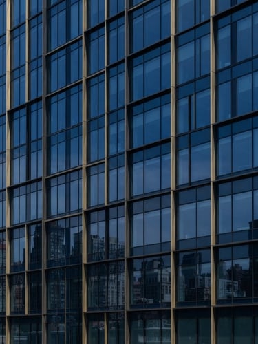 Sharp architectural crop of a modern corporate office building facade, bright natural daylight, clean lines, deep navy glass reflections