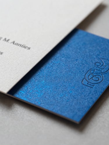 Close-up macro shot of premium textured paper stocks and business card mockups with embossed blue foil details, bright studio lighting, shallow depth of field.