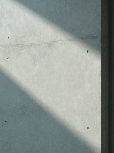 Minimalist architectural detail of a concrete wall and a soft shadow cast by a window frame, cool overcast daylight, desaturated tones