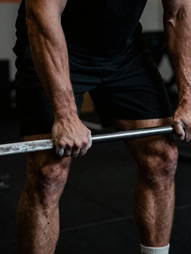 Moody close-up of a male athlete's chalked hands gripping a barbell in a dark, high-contrast gym environment, sharp directional lighting, desaturated tones, 35mm film