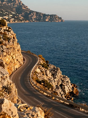 Stunning environmental shot of a coastal road winding along the cliffs near Alanya, bright sun-drenched Mediterranean daylight, deep blue sea.