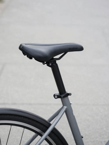 Close-up of a RealSeat comfort saddle mounted on a sleek grey commuter bicycle parked on a clean urban path, soft overcast daylight, desaturated tones, 50mm