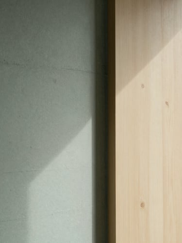 Editorial minimalist photography of a serene architectural detail inside a Hamburg practice, soft shadows on a concrete and light oak wall, clean lines, shallow depth of field.