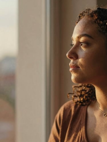 A warm, thoughtful portrait of a queer woman looking out a window, soft golden-hour light, rich earthy tones, 35mm
