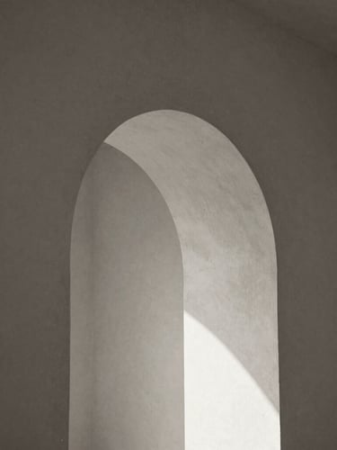 Solitary architectural detail of a concrete archway, abstract soft shadows on a warm plaster wall, minimalist composition, black and white with sepia undertones