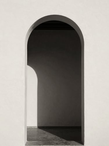 Minimalist architectural archway in Spain, soft natural window light casting deep shadows on a warm cream plaster wall, high contrast black and white photography, sepia undertone, 35mm film grain