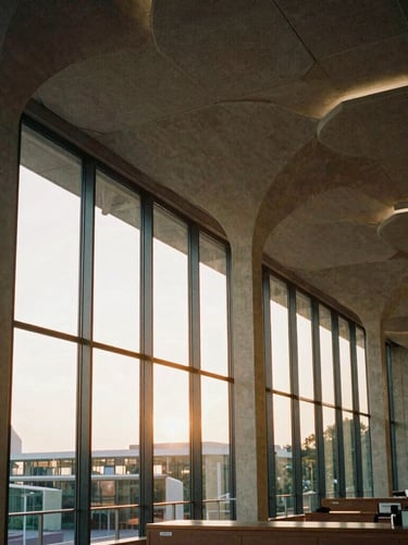 A wide-angle architectural detail of a modern public library with soaring concrete arches and soft golden-hour light filtering through glass, rich textures, warm editorial photography.