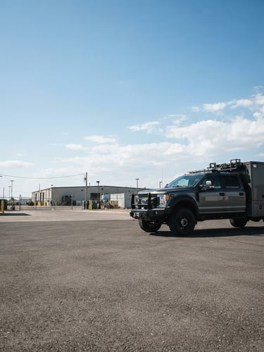 Wide panoramic shot of a clean, branded CASSIDY CONSULTING GROUP fleet vehicle, a heavy-duty tactical truck, parked on a paved lot under crisp natural daylight. The truck is positioned on the right third of the frame, with expansive, clear sky above and a low horizon. High-contrast industrial tones, sharp focus, 35mm lens.
