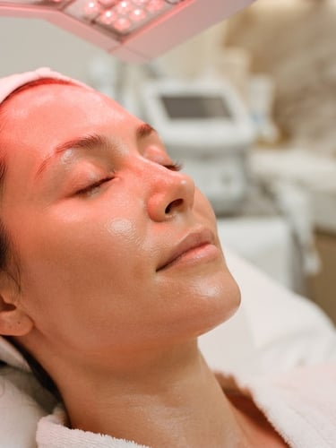 Close-up of radiant, firm skin under a soft red LED phototherapy glow, clinical luxury spa setting, high-end texture, 35mm