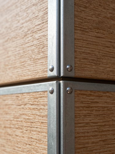 Macro detail of a flush wood-to-steel material junction on a modern residential wall, crisp daylight, sharp focus on the millimeter-precision reveal