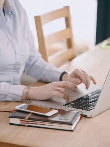 Businesswoman typing on a laptop at a wooden desk with a smartphone and notebook.