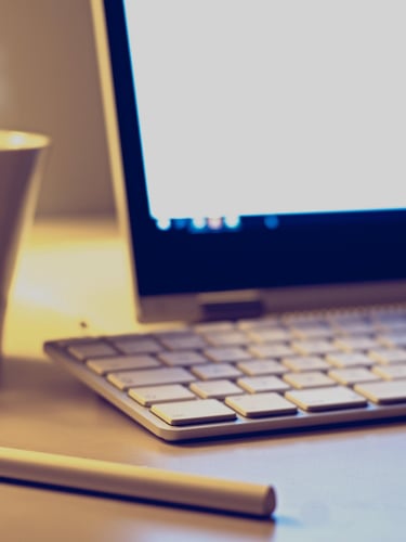 A close-up of a modern home office desk with a laptop, wireless keyboard, stylus pen, and a warm cup of coffee.