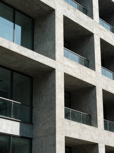 Geometric close-up of a modern concrete facade with glass panels, sharp architectural shadows, bright natural daylight, high contrast, 35mm