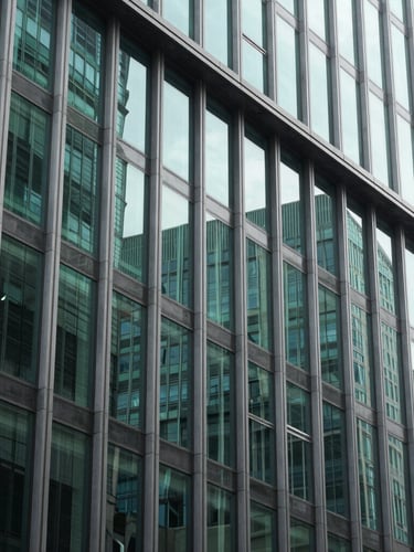 Sharp architectural framing of a modern financial district building facade, high-contrast green glass reflections, bright daylight, 35mm