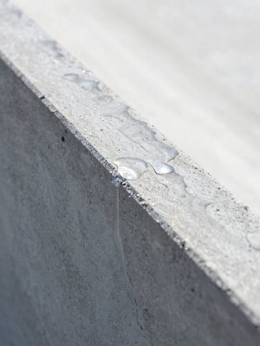 Extreme close-up macro shot of coated structural concrete shedding seawater, superhydrophilic water sheeting, bright direct daylight, high-contrast cool tones, industrial minimalism