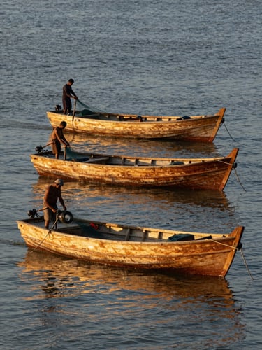 Telephoto compression of two wooden fishing boats stacked in shallow canal distance, fisherman mid-work adjusting nets at the stern, golden-hour light raking across the water surface, muted blue and amber tones
