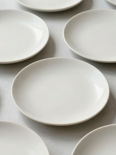 Close-up of elegant finished ceramic plates with delicate pastel brushstrokes, bright editorial photography, soft natural daylight, desaturated pastel tones, clean minimalist setting, 35mm