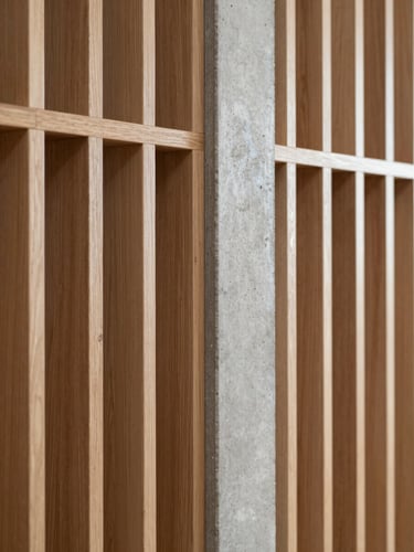 Macro shot of a custom oak timber partition meeting a raw concrete column, illustrating a perfect material junction, soft ambient light.