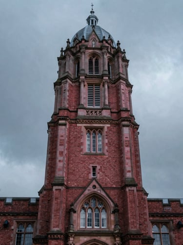 Moody editorial architectural shot of a historic red-brick UK university tower under dramatic overcast grey sky, cool pink tones, 35mm photography.