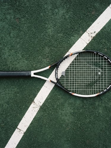 Overhead clean editorial photograph of a professional tennis racket resting on a crisp white court line, deep forest green clay surface, soft morning daylight, 35mm.