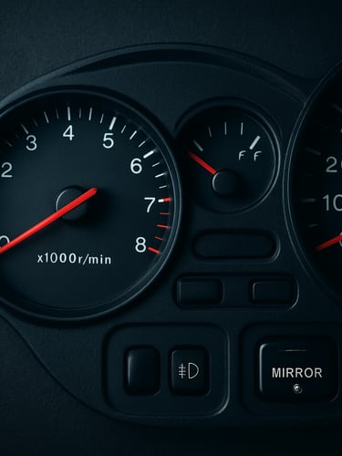 Extreme overhead flat-lay of a car instrument cluster and odometer under cool studio strobe lighting, fuel gauge needle visible mid-frame, dashboard controls in sharp focus, high contrast on dark surface, no people
