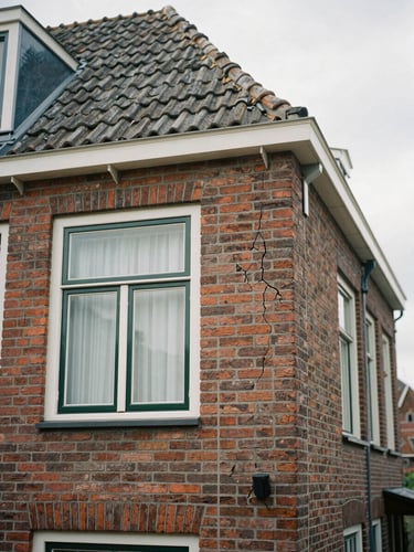 Authentic documentary photo of a traditional brick house in a Drenthe village, soft overcast daylight, focus on subtle structural cracks near a window, 35mm lens