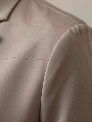 Macro detail shot of a muted taupe silk sleeve seam, showing the precise stitching and luxurious textile texture under soft, indirect daylight.