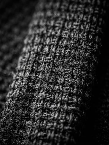 Extreme close-up of a textured black knitted silk tie, sharp focus on the knit grain, high-contrast monochrome photography, deep shadows, 85mm