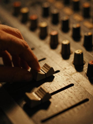Extreme close-up of a hand adjusting a fader on a vintage mixing console, warm amber light glinting off the metal, deep shadows, tactile, 35mm film grain.