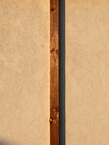 Straight-on architectural elevation of a raw timber joint meeting textured plaster, natural golden-hour sunlight highlighting the tactile transition, medium format film style.