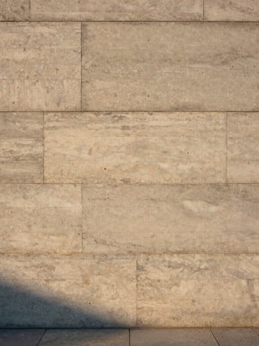 Straight-on architectural elevation of a concrete and raw timber wall, soft golden hour light casting long shadows across textured travertine slabs, medium format film style.