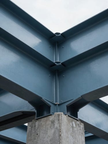 Close-up architectural crop of structural steel beams meeting a concrete foundation, natural high-contrast daylight, cool steel blue and charcoal tones.