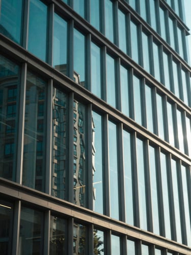 Modern glass office building facade reflecting bright natural sunlight, architectural perspective, deep teal tones, editorial corporate style, shallow depth of field, 35mm