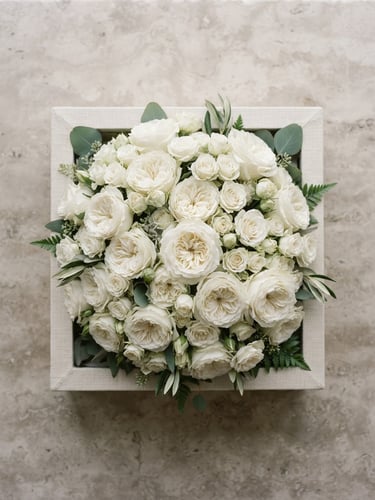 Overhead flat-lay of a sculptural white rose bouquet in a signature linen-wrapped box on a neutral stone backdrop, soft window light, 85mm lens