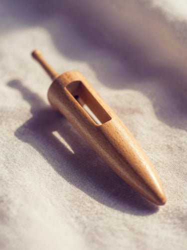 Macro shot of a wooden Hebrew pendulum held gently over clean linen, soft diffused morning light, warm cream and deep purple shadows