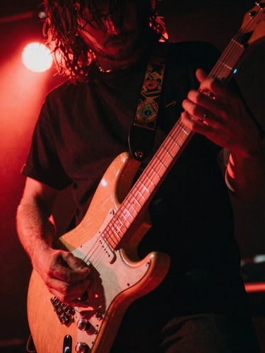 Gritty close-up of a musician's hands playing an electric guitar under harsh red stage lights, motion blur, 35mm film style.