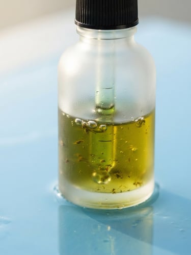 Extreme close-up of raw botanical oils in a frosted glass dropper bottle, soft morning light reflecting on a sky blue surface, macro lens